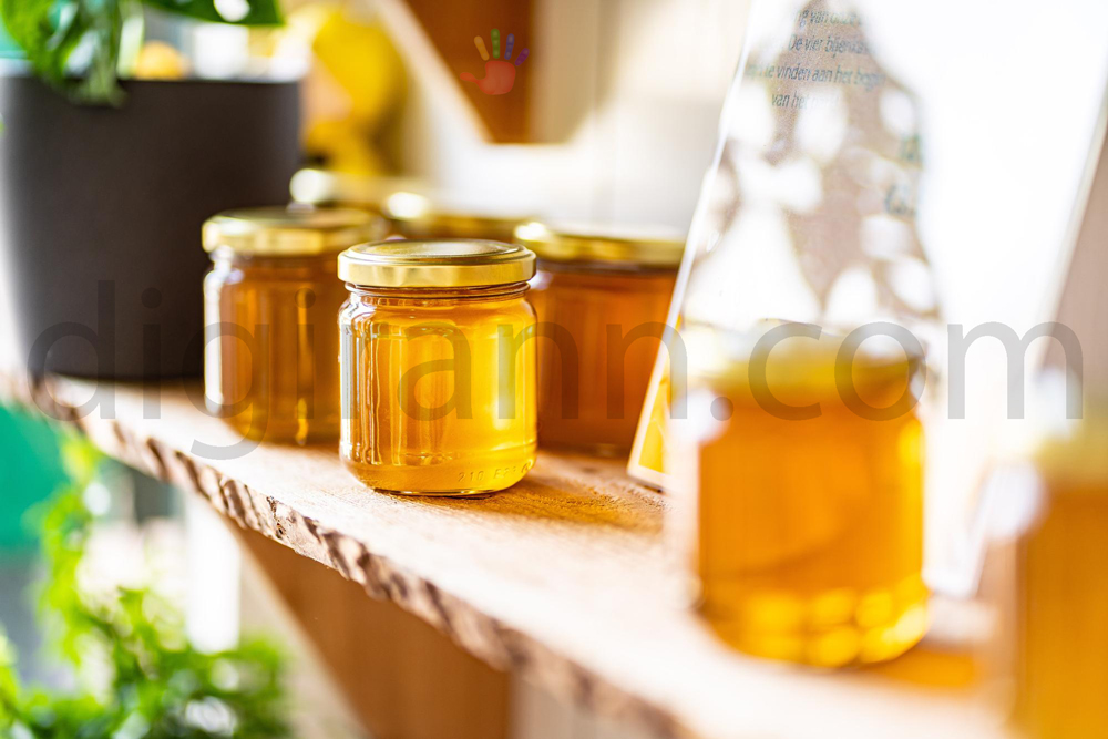 نمایی از انواع ظرف نگهداری عسل چیده شده در قفسه چوبی کنار یک گلدان سبز