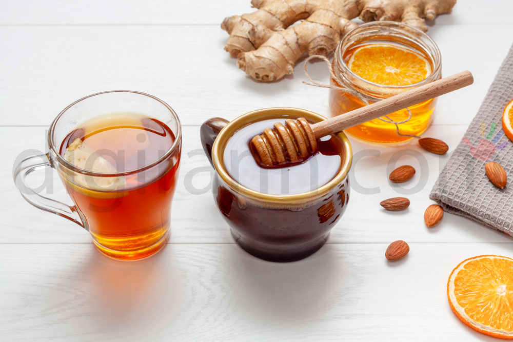 نمایی از ترکیب عسل و آب گرم و لیمو ترش و تعدادی بادام با یک قاشق چوبی عسل و لیوان چای روی میز چوبی