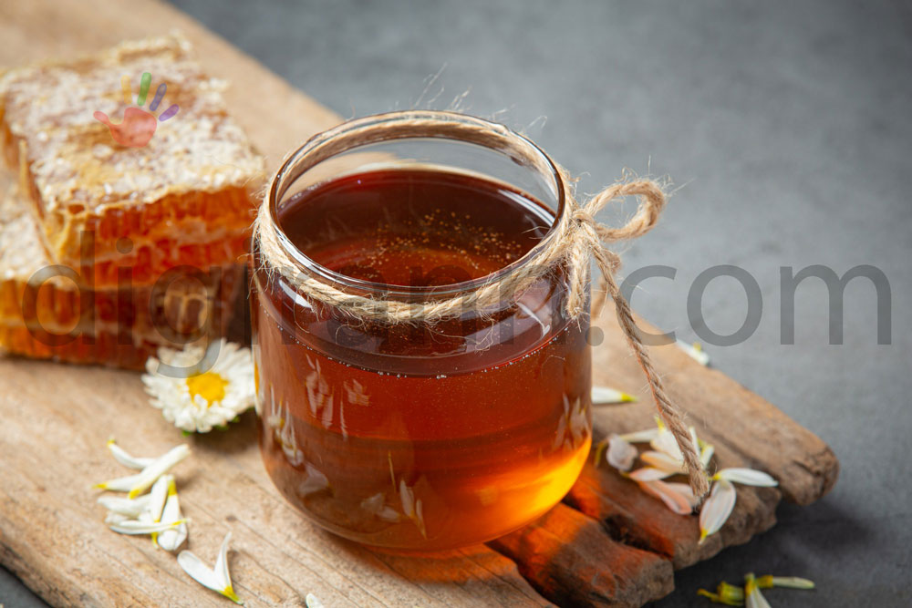 نمایی از خواص عسل چهل گیاه روی تخته چوب در کنار گل پرپر و تکه های موم