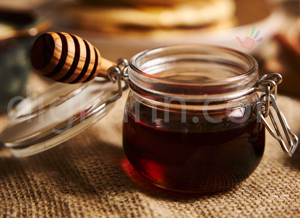 نمایی از خواص عسل سیاه در ظرف شیشه ای کوچک با قاشق چوبی روی نمد