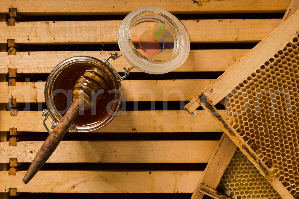 نمایی از رنگ عسل سیاه در ظرف شیشه ای در کنار دو قاب موم عسل شان موم روی کندو