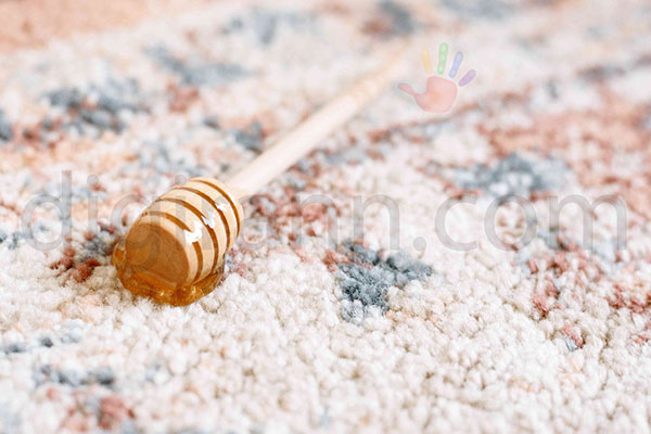 نمایی از ریختن عسل روی فرش با یک قاشق چوبی عسلی