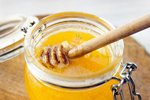 نمایی از ظرف شیشه ای عسل کرستالیزه شده زرد با قاشق چوبی عسل در آن